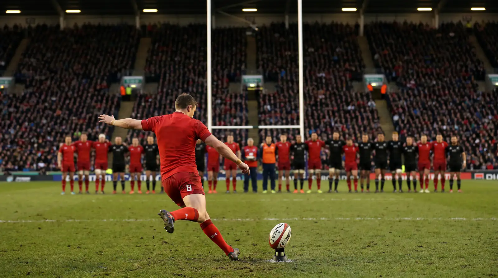 Rugby union goal-kicker stepping into a conversion attempt at the posts with stadium crowd watching