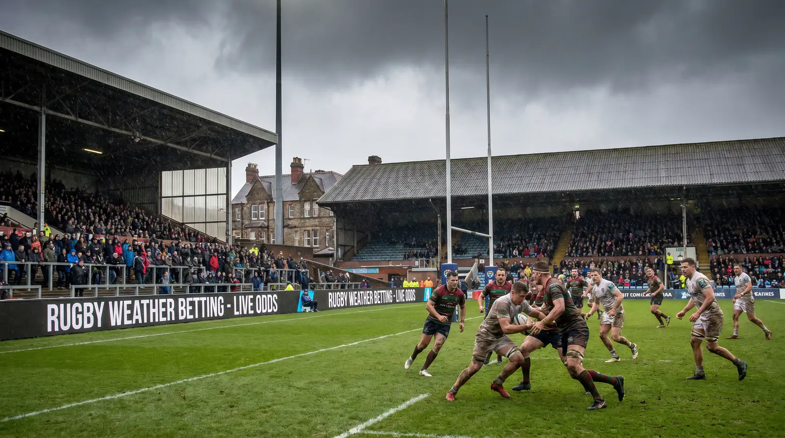 Iconic UK rugby stadium with windswept open stand on match day